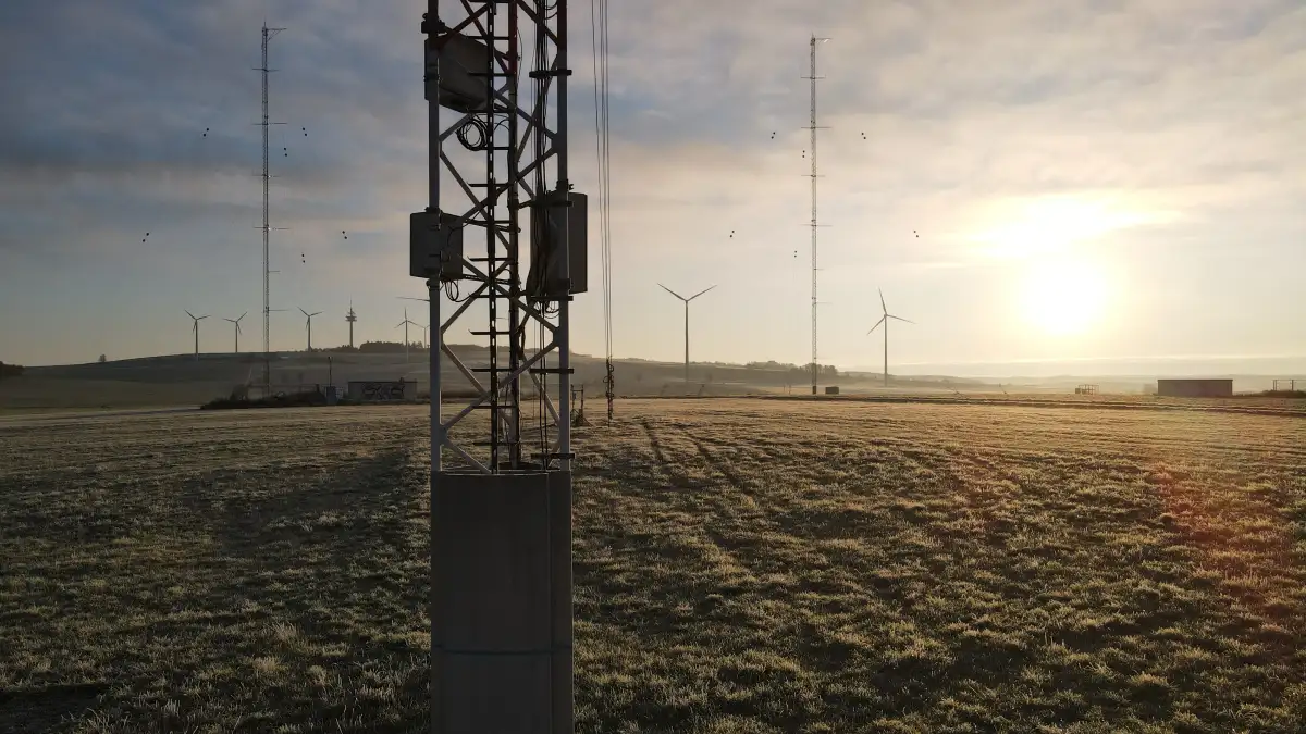 Close-up of a met mast against the light with other met masts and wind turbines in the background.