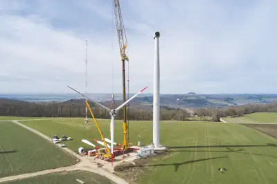 Drohnenaufnahme von der Errichtung einer Windenergie. Ein Kran hebt den Rotorstern an.